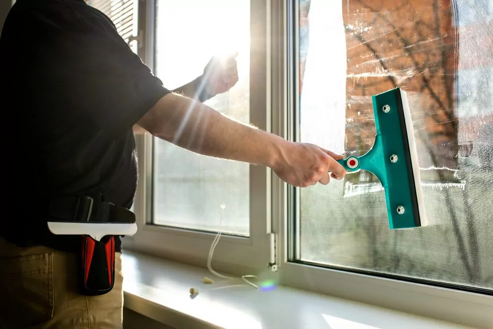 Hand mit Abzieher reinigt eine Fensterscheibe streifenfrei